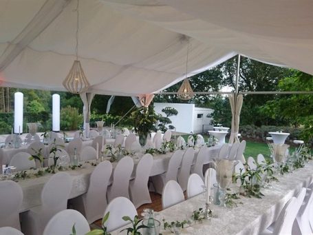 Elegante Tafeln mit weißen Stühlen und Blumenarrangements in einem Festzelt mit geöffneten Seiten im privaten Garten.
