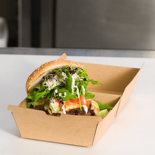 Burger mit Salat, Tomate und Saucen in einer Pappschachtel serviert.