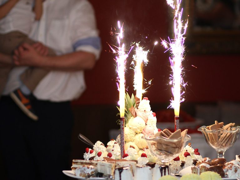 Eisbombe mit Tischfeuerwerk, im Hintergrund ein Kind auf dem Arm eines Erwachsenen.