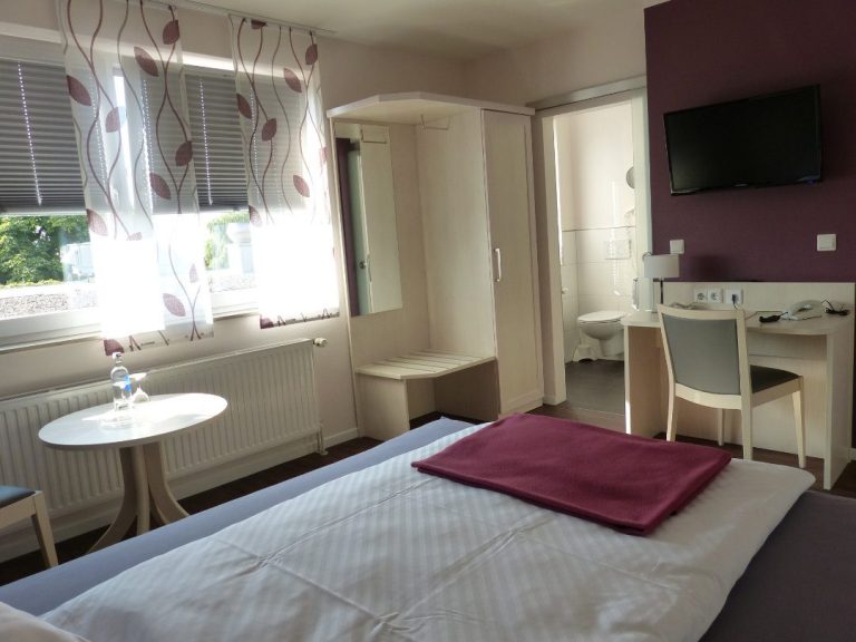Ein modernes Einzelzimmer mit Blick vom Bett auf einen Schreibtisch, einen Flachbildfernseher und das Badezimmer.