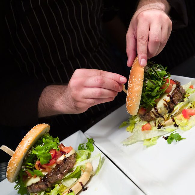Ein Burger wird mit frischem Salat, Tomaten und einer Sesambrötchenhaube angerichtet.