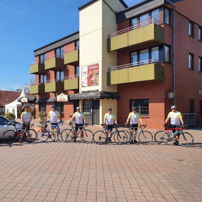 Eine Gruppe von Fahrradfahrern präsentiert bei schönem Wetter vor dem Hotel ihre neuen Trikots.