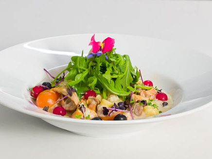 Bunte Salatvariation mit Kräutern, Beeren und essbaren Blüten auf weißem Teller.