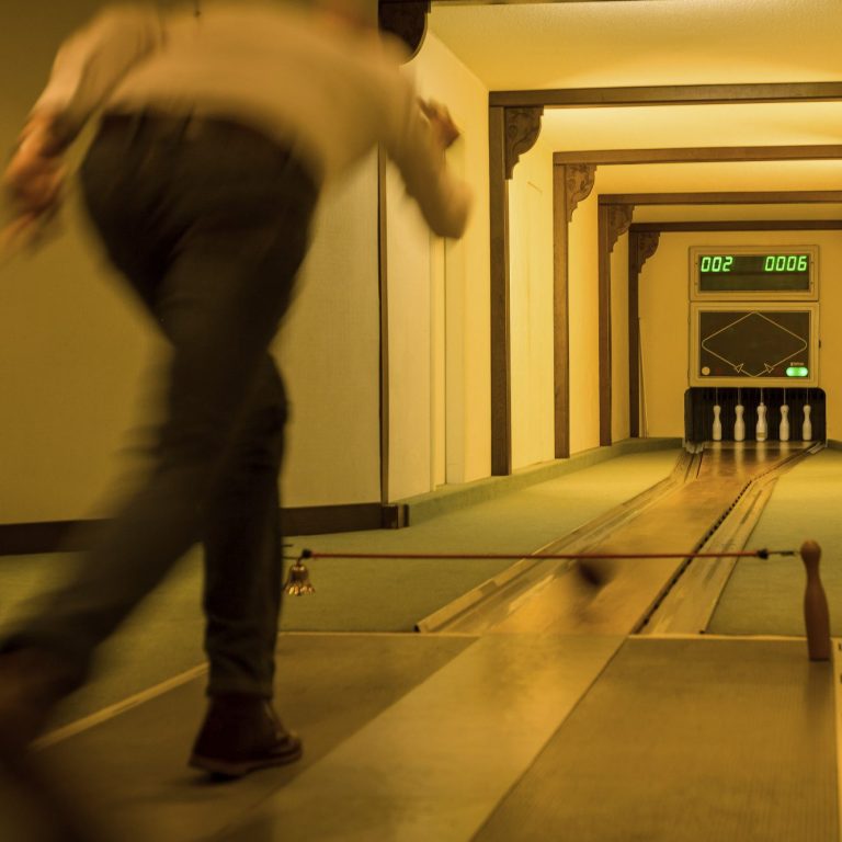 Person wirft einen Kugel auf eine Bahn mit Kegeln im Hintergrund.
