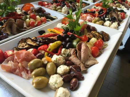 Bunt angerichtete Platten mit Antipasti: Oliven, Aufschnitt, Käse, Gemüse und frische Kräutern.