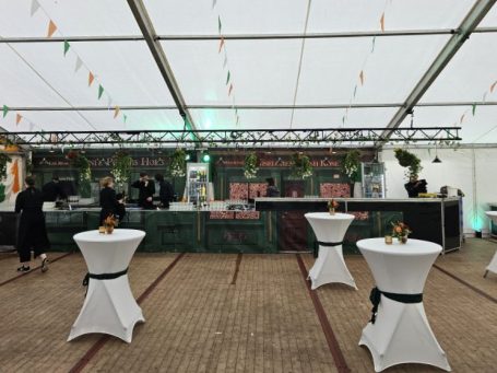 Barbereich in einem Partyzelt mit Stehtischen und grüner Dekoration für eine Veranstaltung.