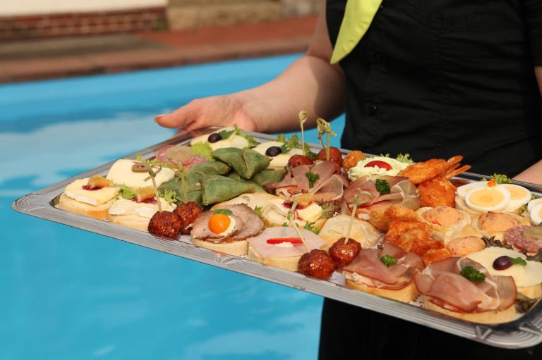 Hände tragen ein Tablett mit verschiedenen appetitlichen Häppchen und Finger-Food.