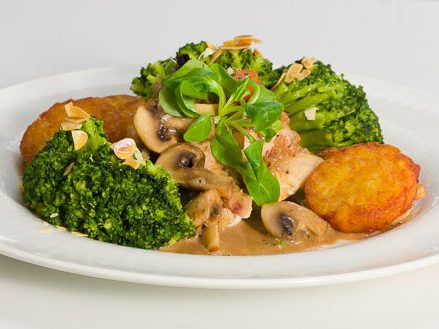 Gericht mit Fleisch, Kartoffelrösti, Brokkoli und Champignons auf einem weißen Teller.