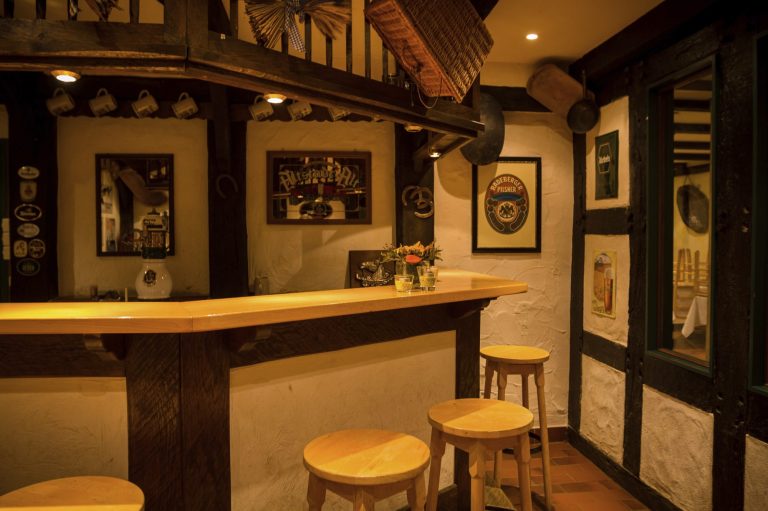 Rustikale Holztheke mit Barhockern in einem Partykeller. Historische Schilder und Spiegel als Wanddekoration.